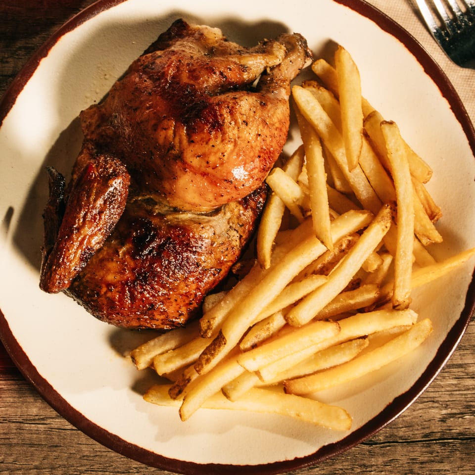 Grilled chicken pieces and golden fries served on a white plate atop a wooden restaurant table.