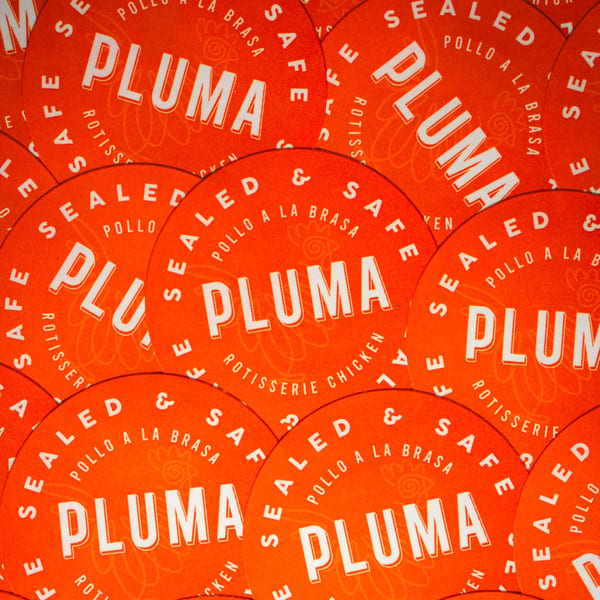 Overlapping orange circular stickers for Pluma restaurant, featuring "Pollo a la Brasa" and "Rotisserie Chicken".
