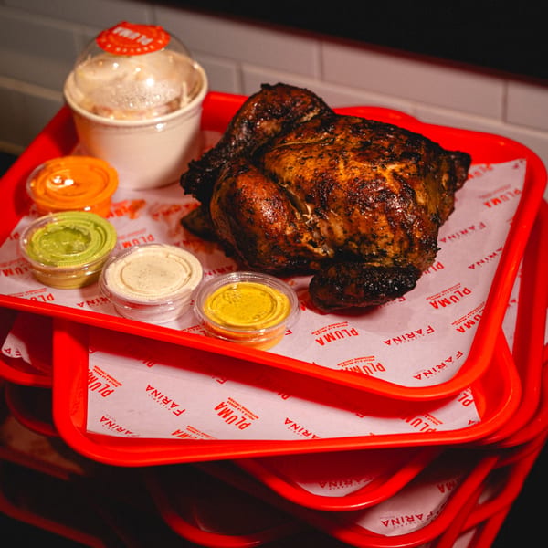 A whole roasted chicken, four dipping sauces, and a side dish on a red tray.